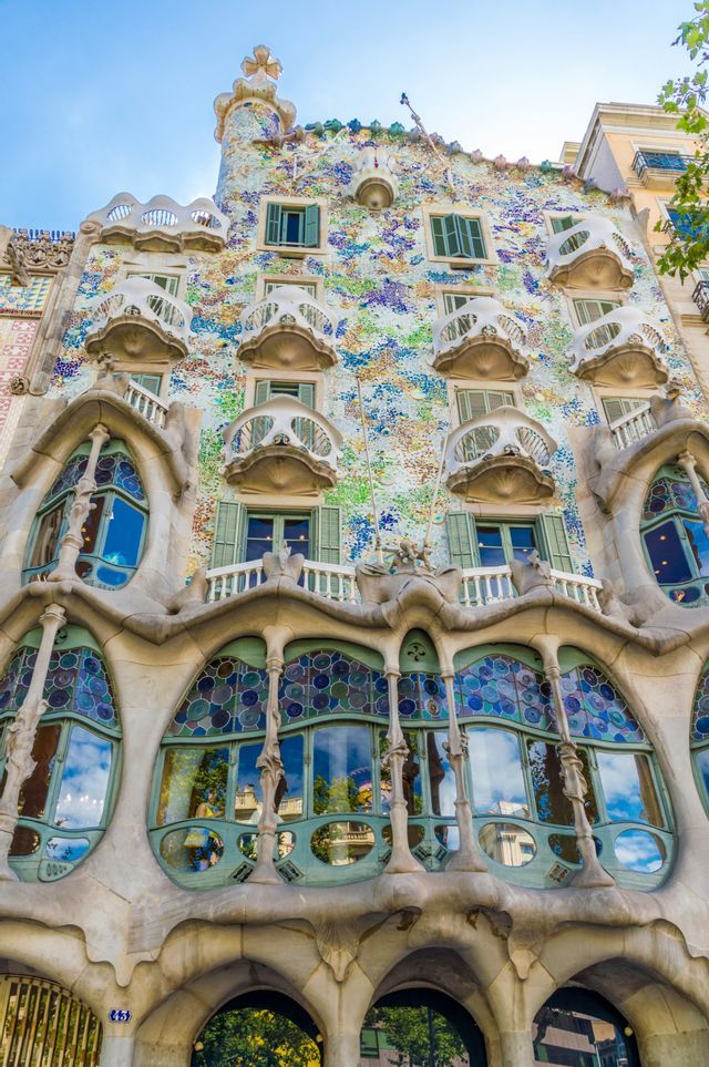 Un'inquadratura dal basso di una facciata di edificio con un mosaico colorato, pilastri a forma di osso e balconi che ricordano teschi.