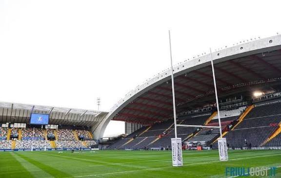 Pali da rugby si ergono su un campo verde in un grande stadio con un tetto curvo, visti dal livello del campo.