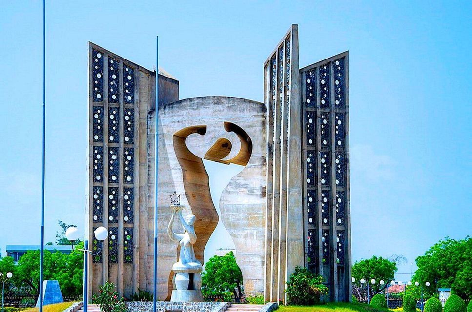 Un monumento moderno in cemento che presenta una grande figura astratta e una statua più piccola che tiene una stella, situato in un parco verde.