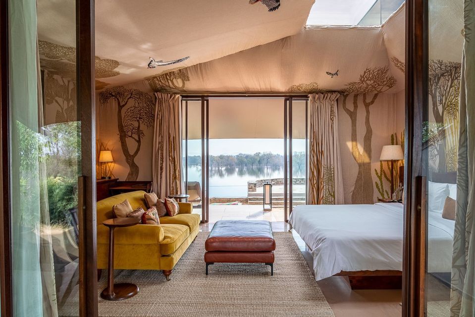 Una tenda di lusso con divano giallo e letto, dotata di porte a vetri che si aprono su una serena vista sul lago.