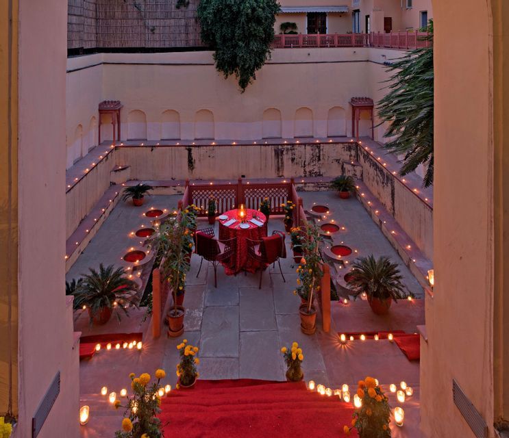 Un tavolo da cena intimo allestito in un cortile ribassato, illuminato da decine di candele accese e circondato da piante.
