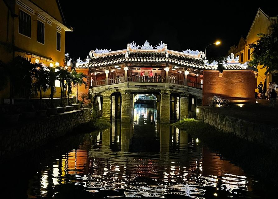 Un ponte coperto decorato, illuminato di notte, con le sue luci che si riflettono sull'acqua sottostante.