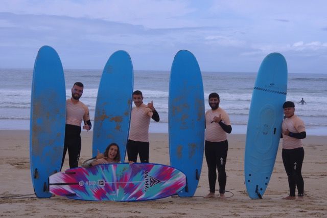 Un gruppo di viaggio WeRoad sorride e posa con le proprie tavole da surf su una spiaggia sabbiosa di fronte all'oceano.