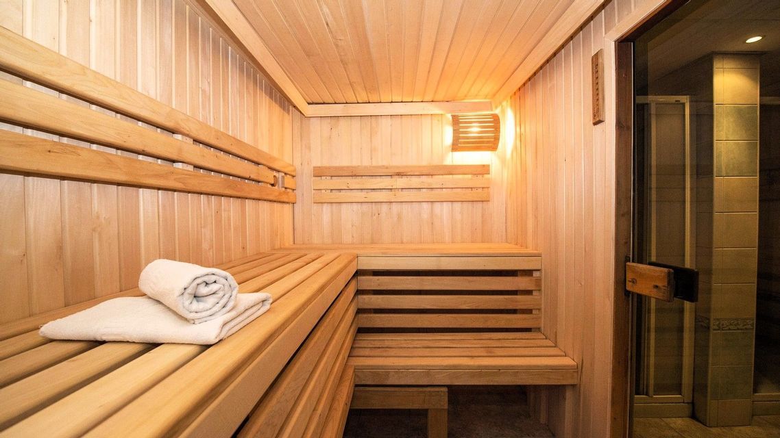 Weiße Handtücher liegen auf einer Holzbank in einem leeren, warm beleuchteten Saunaraum mit gestuften Sitzgelegenheiten.