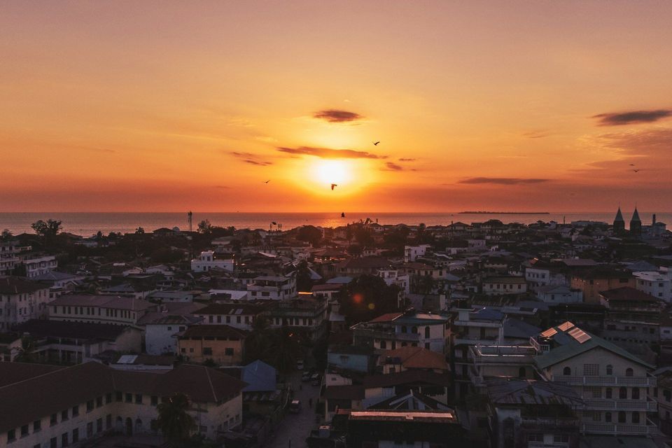 Un tramonto arancione sull'oceano illumina i tetti di una città di mare.