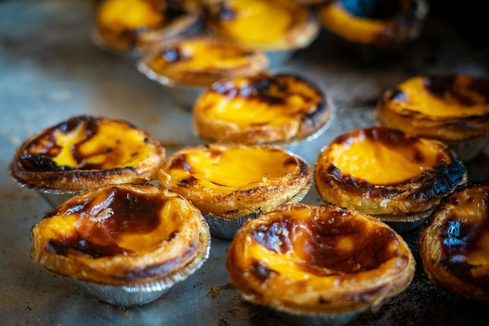 Nahaufnahme mehrerer frisch gebackener portugiesischer Puddingtörtchen, bekannt als Pastéis de Nata, auf einem Metallbackblech.
