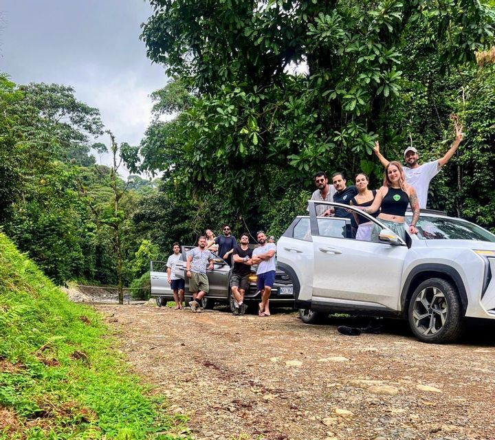Un viaggio di gruppo WeRoad in posa con due auto su una strada sterrata circondata da una fitta giungla verde.