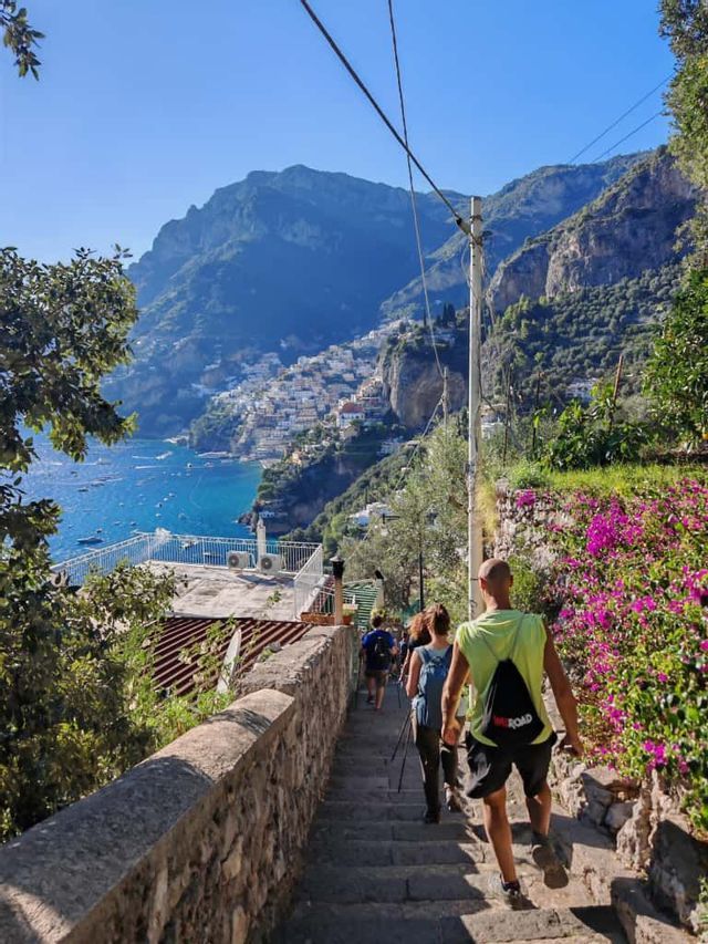 Un viaggio di gruppo WeRoad scende una scalinata in pietra con vista su una città a picco e un mare blu.
