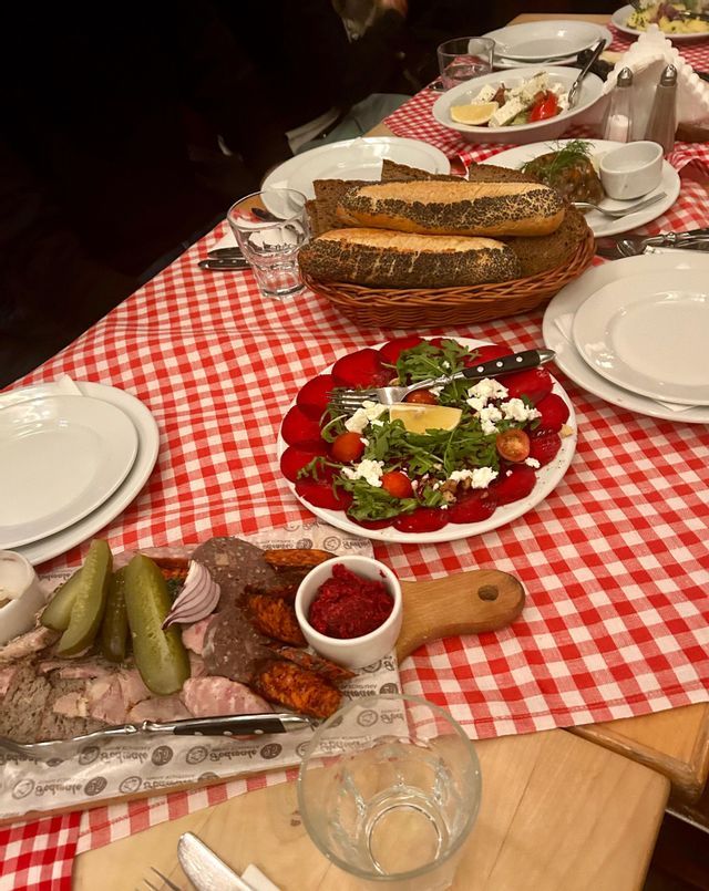Une table avec une nappe à carreaux rouges et blancs est dressée avec une planche de charcuterie, une salade de betteraves et un panier de pain.