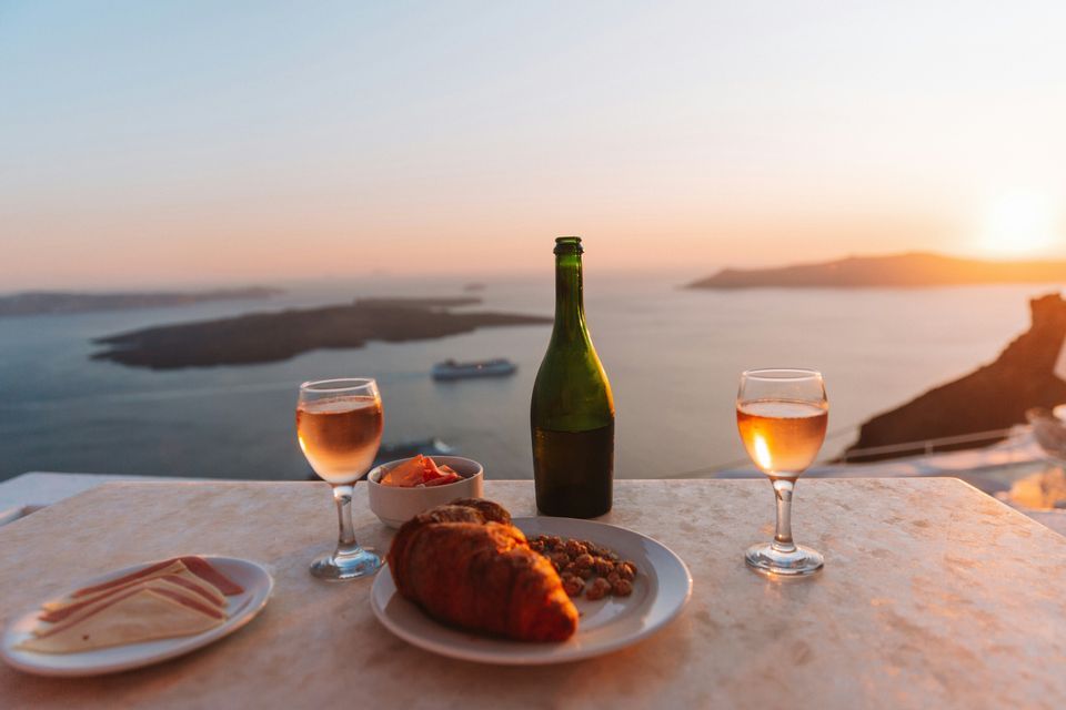 Un aperitivo con due calici di vino rosato e un croissant su un tavolo vista mare al tramonto.