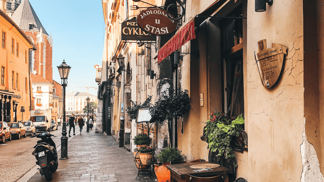 Uno scooter è parcheggiato su una stretta strada di ciottoli fiancheggiata da edifici storici, con un'antica torre di chiesa visibile sullo sfondo.