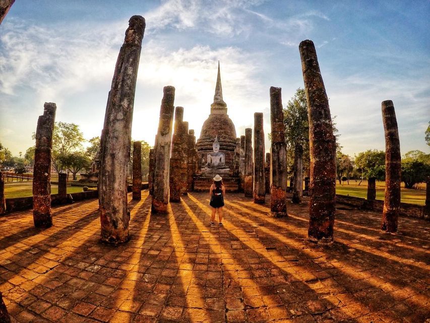 Ein Mädchen mit dem Rücken zu den Ruinen eines thailändischen Tempels - WeRoad