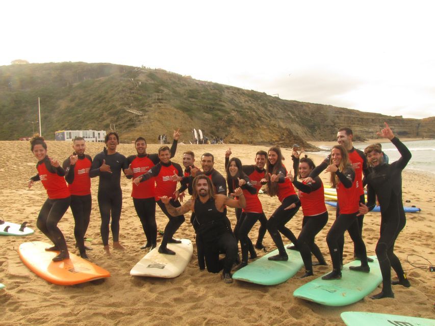 Un viaggio di gruppo WeRoad in muta, mentre posano giocosamente su tavole da surf su una spiaggia sabbiosa.