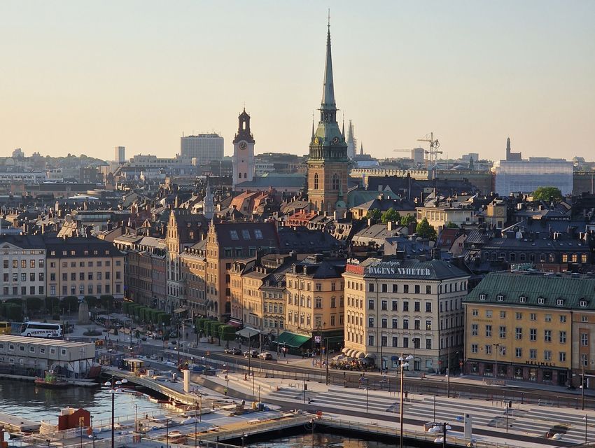 Veduta dall'alto dello skyline di una città storica europea, con un campanile di chiesa e il lungomare, durante una calda alba.