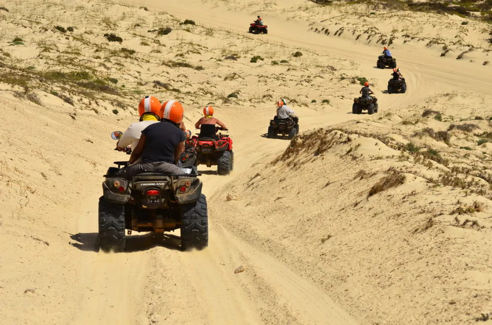 Un viaggio di gruppo WeRoad in quad, in fila su una pista sabbiosa tra dune ondulate.
