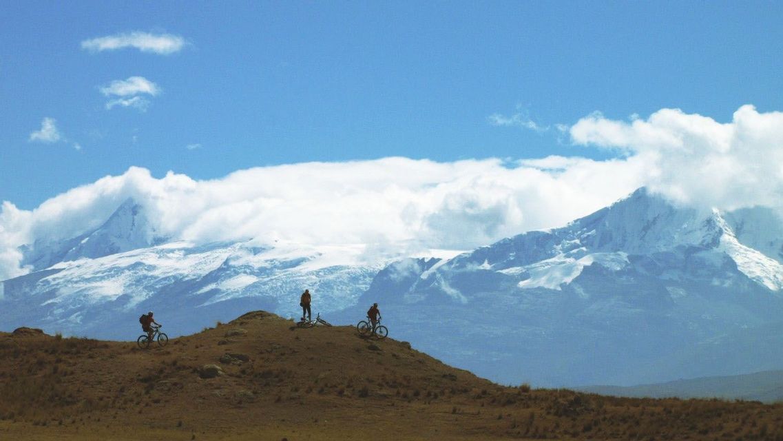 Sagome di un viaggio di gruppo WeRoad con mountain bike su una collina con lo sfondo di montagne innevate.