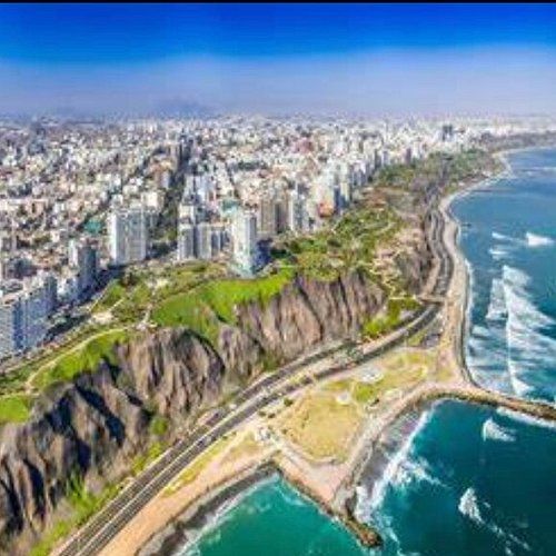 Una vista aerea di una vasta città costiera arroccata su alte scogliere erbose accanto all'oceano sotto un cielo azzurro e limpido.