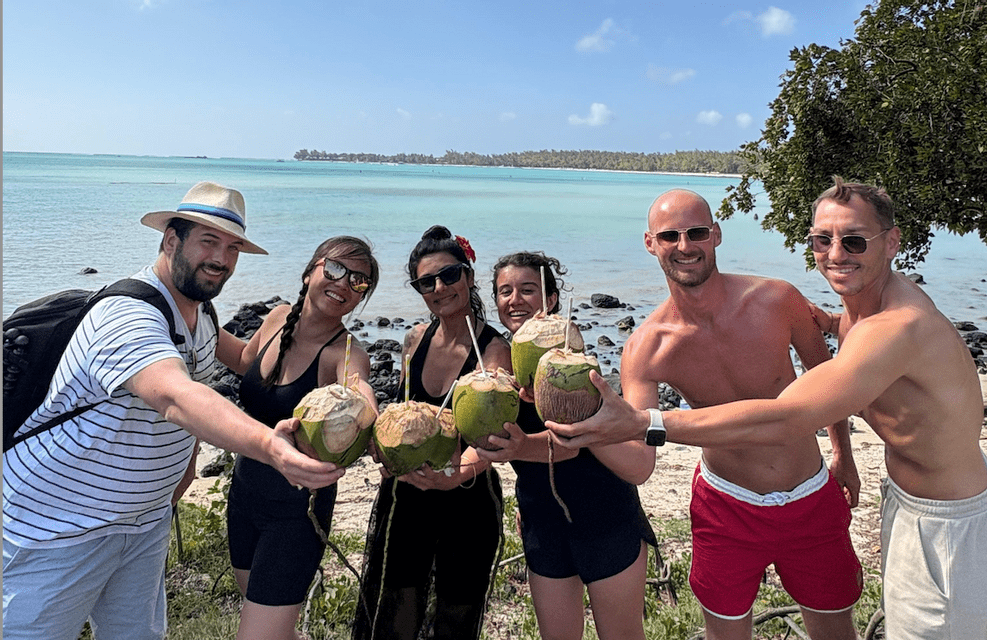 Un voyage de groupe WeRoad avec des personnes souriantes tenant des noix de coco fraîches sur une plage au bord de la mer turquoise.