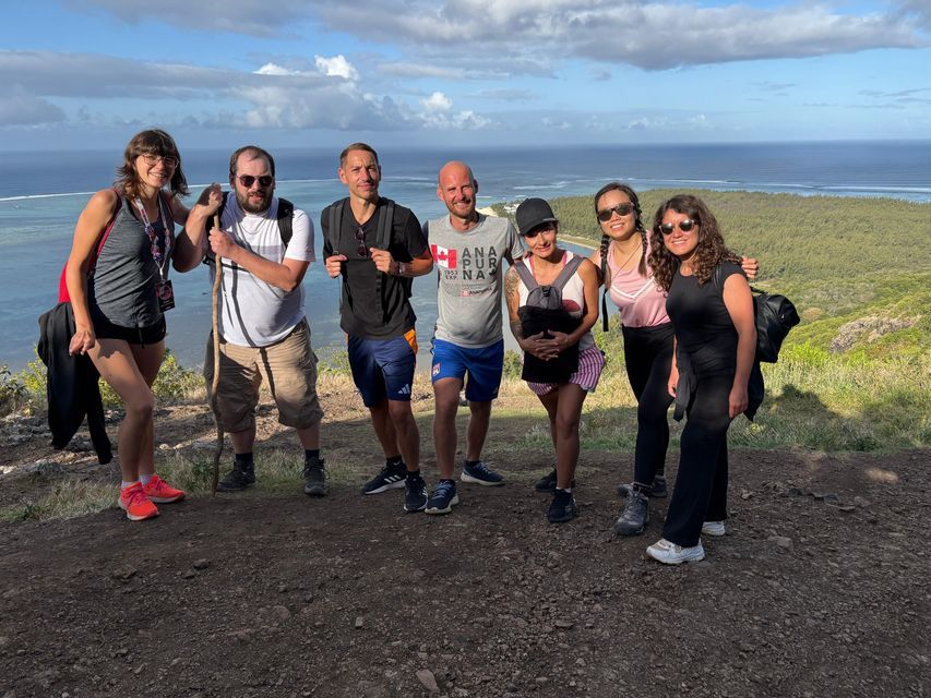 Un voyage de groupe WeRoad de sept personnes posant pour une photo sur un chemin de terre surplombant l'océan et une côte verdoyante.