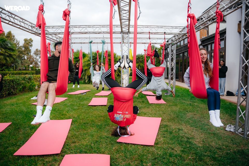 Un gruppo WeRoad pratica yoga aereo su amache rosse sospese su un prato verde.