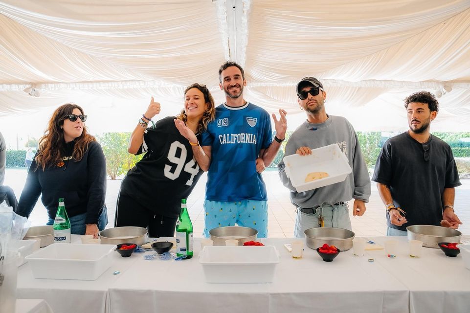 Un viaggio di gruppo WeRoad di cinque persone che posano per una foto durante quella che sembra essere una lezione di cucina sotto una tenda bianca.