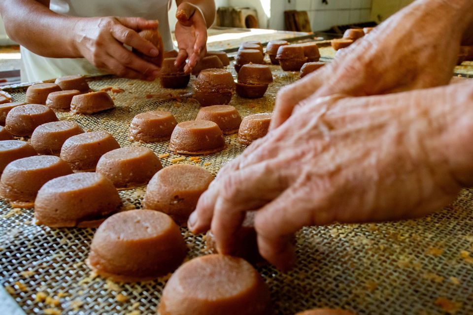 Gros plan sur les mains de deux personnes qui préparent de petites douceurs marron en forme de dôme sur un plateau métallique grillagé.
