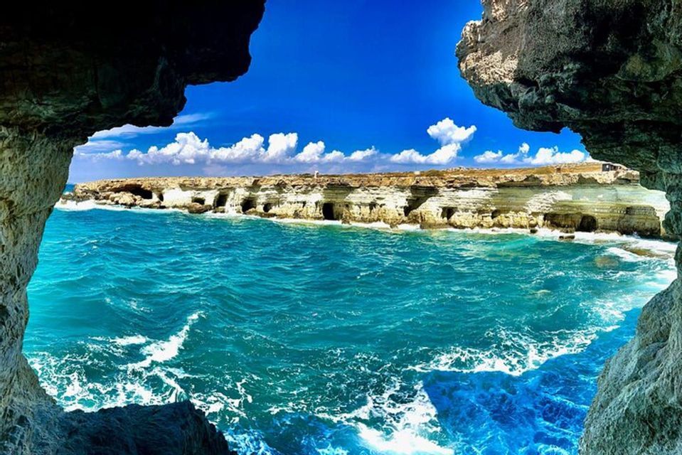 Vue de l'intérieur d'une grotte marine donnant sur un littoral rocheux avec d'autres grottes marines, un océan turquoise et un ciel bleu nuageux.