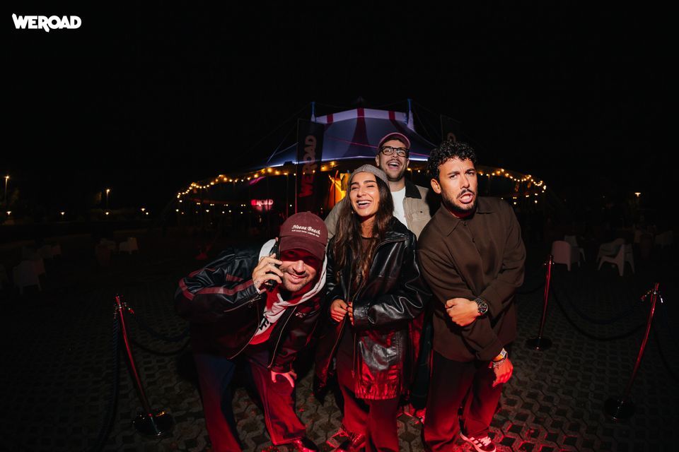Un gruppo WeRoad di quattro persone ride e posa per una foto di notte davanti a una grande tenda per eventi illuminata.