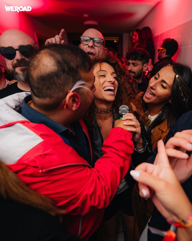 Un viaggio di gruppo WeRoad con persone che ridono e cantano al karaoke insieme in un corridoio con luci rosse.