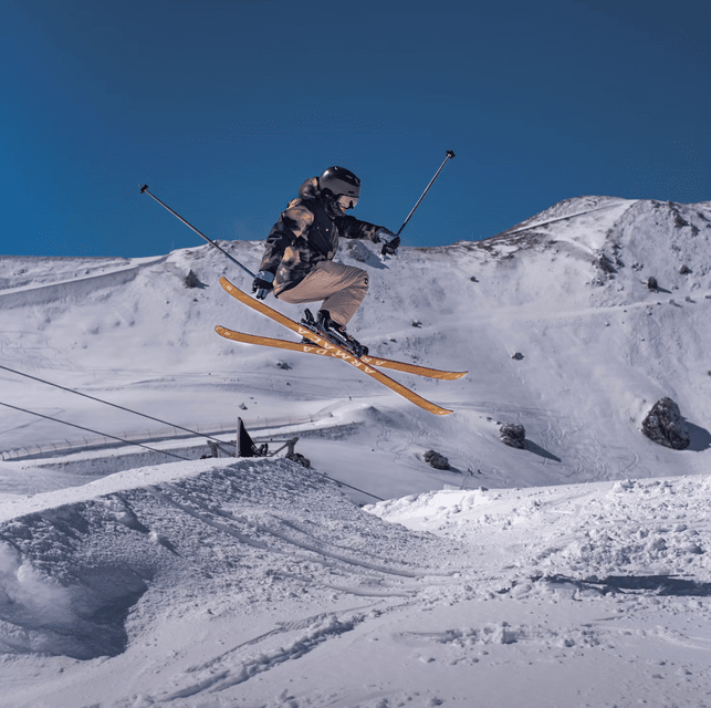 Un skieur s'élance en l'air depuis une rampe de neige sur une pente de montagne sous un ciel bleu dégagé.