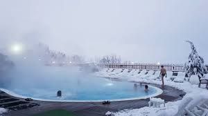 Unas pocas personas se relajan en una piscina exterior de agua caliente rodeada por un paisaje completamente cubierto de nieve.