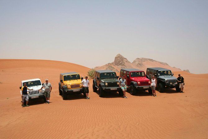 Un viaggio di gruppo WeRoad in posa con una fila di veicoli fuoristrada colorati su vaste dune di sabbia nel deserto sotto un cielo sereno.