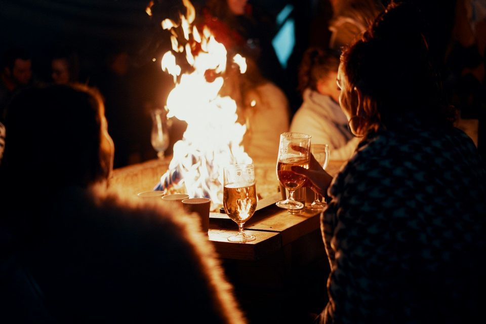 Eine WeRoad-Gruppe versammelt sich nachts um ein Lagerfeuer, mit Biergläsern auf dem Tisch.