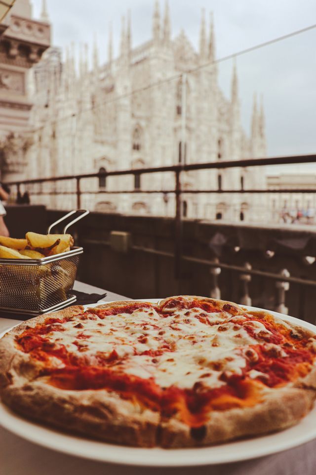 A margherita pizza and a basket of fries on a table, with a large Gothic cathedral out of focus in the background.