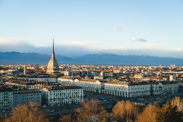 A dense cityscape featuring a prominent spire, with a distant snow-capped mountain range visible under a clear sky.