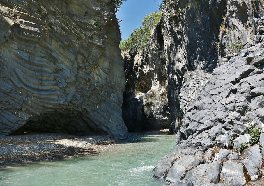 Un fiume dalle acque verde chiaro si snoda attraverso un canyon di roccia vulcanica stratificata e colonnare in una giornata di sole.