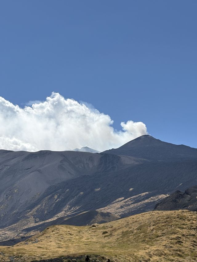 Un gruppo WeRoad percorre un sentiero erboso con un grande vulcano fumante sullo sfondo, sotto un cielo azzurro.
