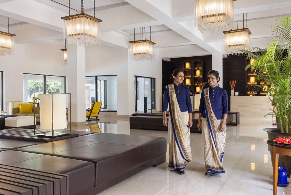 Zwei lächelnde Hotelmitarbeiterinnen in traditionellen Uniformen gehen durch eine helle, moderne Hotellobby.