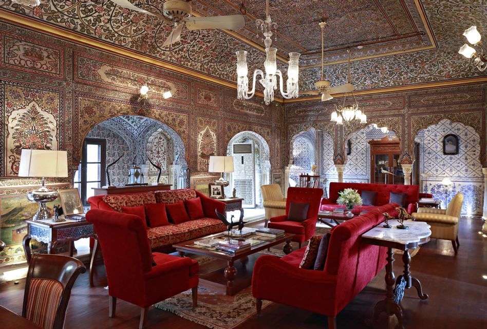 Una sala ricamente decorada con sofás de terciopelo rojo, paredes y techo intrincadamente pintados, puertas arqueadas y arañas de cristal colgantes.