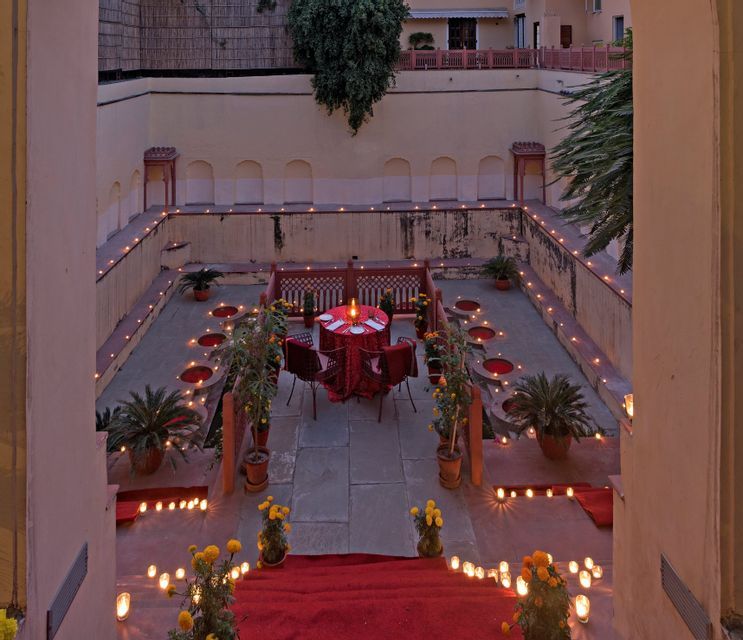 Una mesa de comedor para cuatro con un mantel rojo en un patio de piedra hundido, iluminada por docenas de velas.