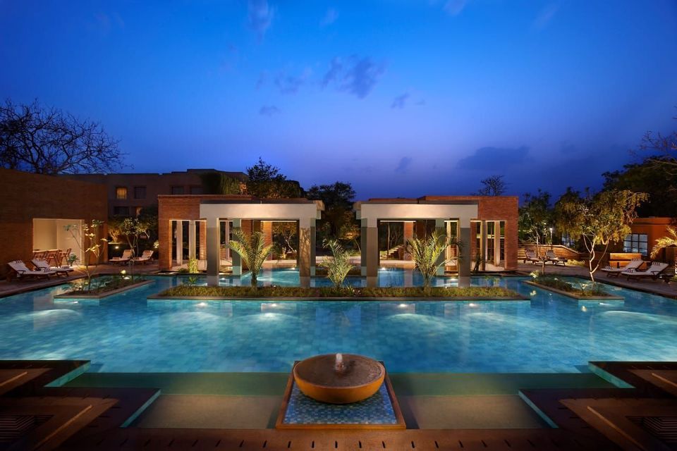 Ein Resort-Swimmingpool, der in der Dämmerung von Unterwasserlichtern beleuchtet wird, mit zwei modernen Pavillons und Liegestühlen am Pooldeck.