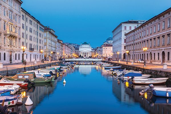 Un canale cittadino con piccole imbarcazioni ormeggiate lungo edifici storici illuminati al tramonto, con riflessi nell'acqua calma.