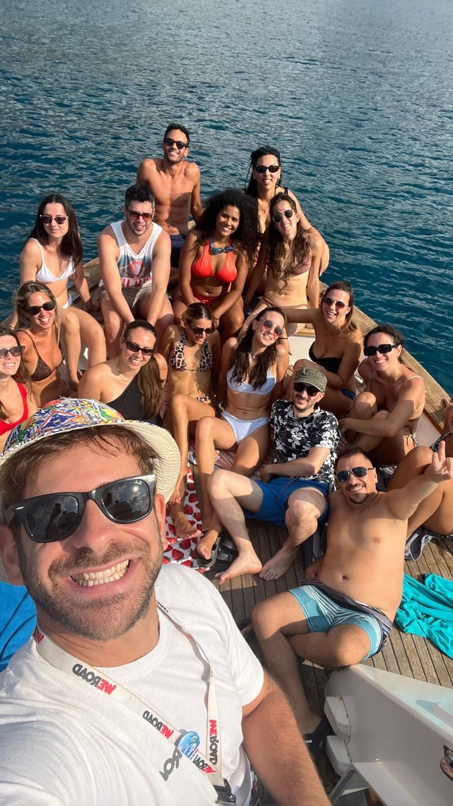 Un viaggio di gruppo WeRoad in costume da bagno, sorridenti per un selfie sul ponte di legno di una barca circondata da acqua blu.