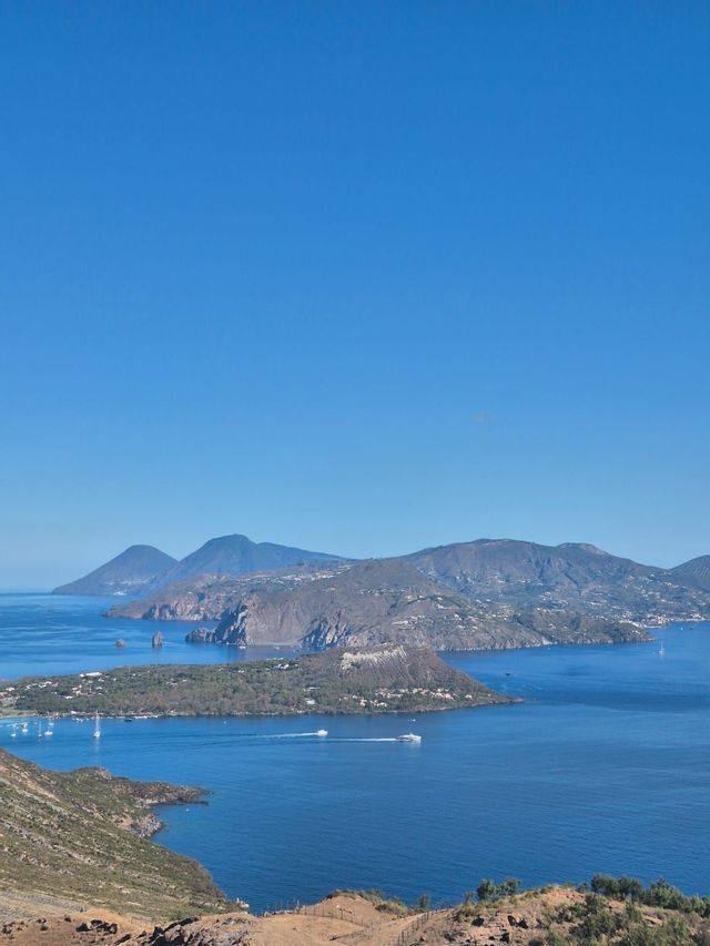 Una vista dall'alto di un arcipelago di isole montuose in un vasto mare blu, con diverse imbarcazioni sull'acqua sotto un cielo limpido.