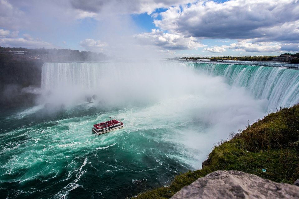 Una barca turistica con un gruppo WeRoad naviga tra le acque nebbiose e turchesi ai piedi di una potente cascata.