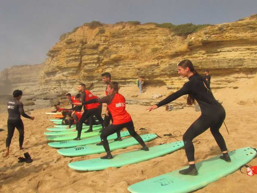 Un viaggio di gruppo WeRoad con lezione di surf su una spiaggia sabbiosa, imparando a stare in piedi sulle tavole da surf di fronte a una scogliera.
