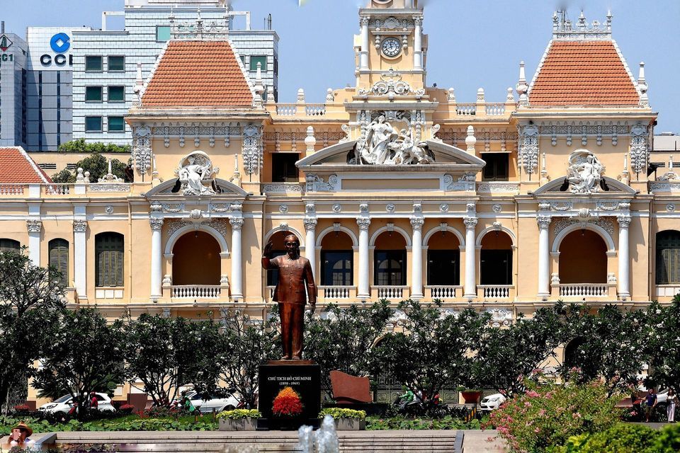 Una statua di bronzo di una figura politica si trova in un giardino di fronte all'ornato e giallo palazzo del Municipio di Ho Chi Minh.