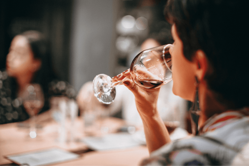 Primo piano di una persona durante un viaggio di gruppo WeRoad che beve vino rosso da un bicchiere a tavola.