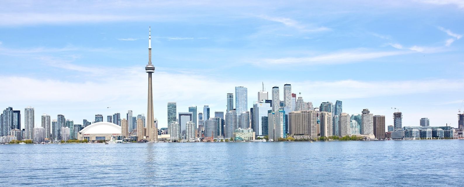 Uno skyline moderno con un'alta torre di osservazione e grattacieli, visibile dall'acqua sotto un cielo azzurro e limpido.
