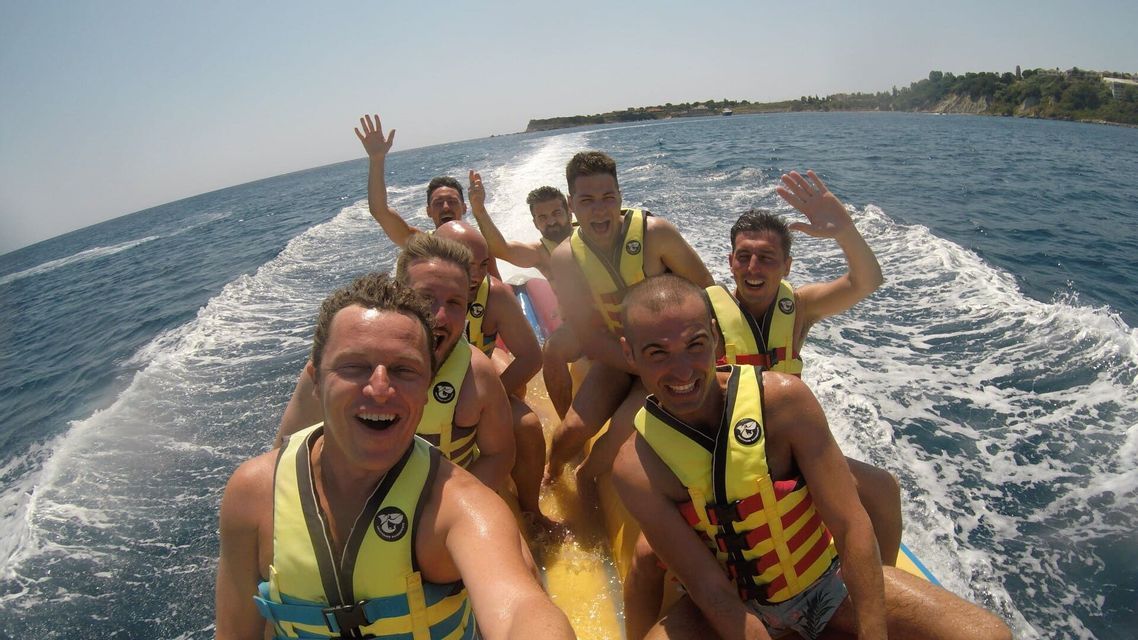 Un viaggio di gruppo WeRoad con uomini che ridono e si scattano un selfie mentre sono su un gommone a banana giallo in mare.